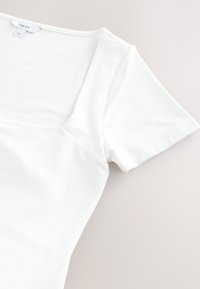 T-shirt blanc à manches courtes avec un décolleté carré, fabriqué en matière douce, présentant une coupe ajustée et un détail de couture minimaliste.