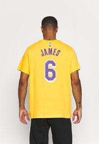 Żółta bawełniana koszulka z fioletowymi napisami. Na plecach znajduje się napis "JAMES" nad numerem "6" w wyrazistym wzorze.