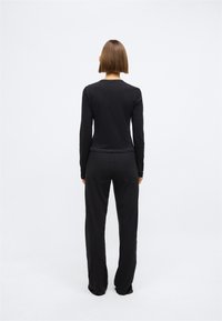 Blusa preta de manga longa com decote redondo, combinada com calças largas pretas, ambas feitas de um tecido suave e liso.