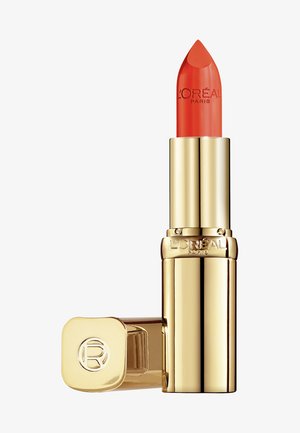 Rossetto arancione in un astuccio cilindrico dorato con una finitura elegante. Capsula con un dettaglio del logo circolare, che mostra il nome del marchio impresso sul lato.