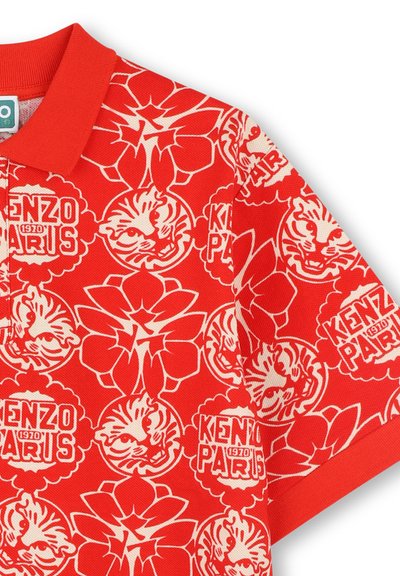 T-shirt polo rouge avec un motif intégral de fleurs blanches et de motifs de tigre, avec le texte "KENZO PARIS" intégré dans le design.