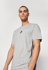 T-shirt en coton gris à manches courtes, avec un logo noir sur la poitrine et des panneaux latéraux noirs contrastants pour une touche de détail supplémentaire.