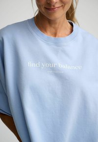 Lichtblauwe sweatshirt met een relaxte pasvorm, voorzien van een ronde halslijn en bedrukte tekst "vind je balans" in het wit. Zachte, gestructureerde stof.