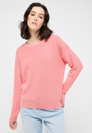Helles rosa Sweatshirt mit geripptem Muster, rundem Ausschnitt und lockerer Passform. Kombiniert mit hellblauen Jeans, die ein dezentes Logo-Detail aufweisen.