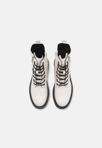 Světlé béžové kotníkové boty s černými tkaničkami, bočními zipy a gumovými podrážkami. Hladká kožená svršek a polstrovaný interiér pro pohodlí.