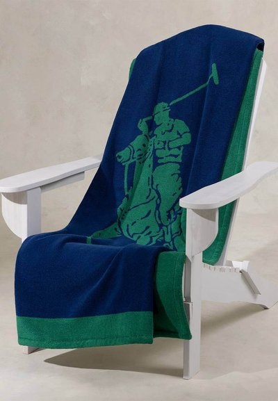Άσπρη ξύλινη καρέκλα με μπλε ναυτικό και πράσινο κουβέρτα που φέρει το πράσινο σιλουέτα ενός παίκτη πόλο που κρατάει ρόπαλο, απλωμένη στην πλάτη και στο κάθισμα.