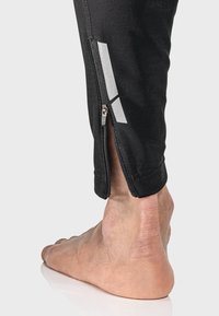 Schwarze Sporthosen mit Knöchelreißverschlüssen und reflektierenden Akzenten. Das Material wirkt glatt und dehnbar, geeignet für aktive Bekleidung.