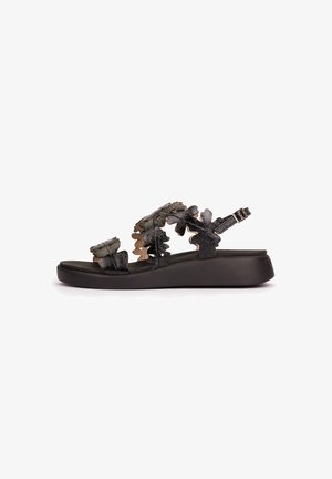 Black open-toe sandal with leaf-shaped leather straps and an adjustable ankle buckle on a slightly elevated sole.
