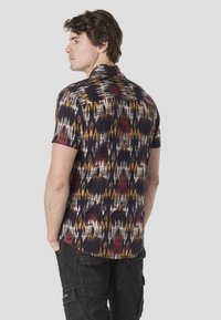 Košeľa s krátkym rukávom s viacfarebným abstraktným vzorom v tmavých tónoch, s kempovým golierom a rovnými lemami. Materiál pôsobí ľahko.
