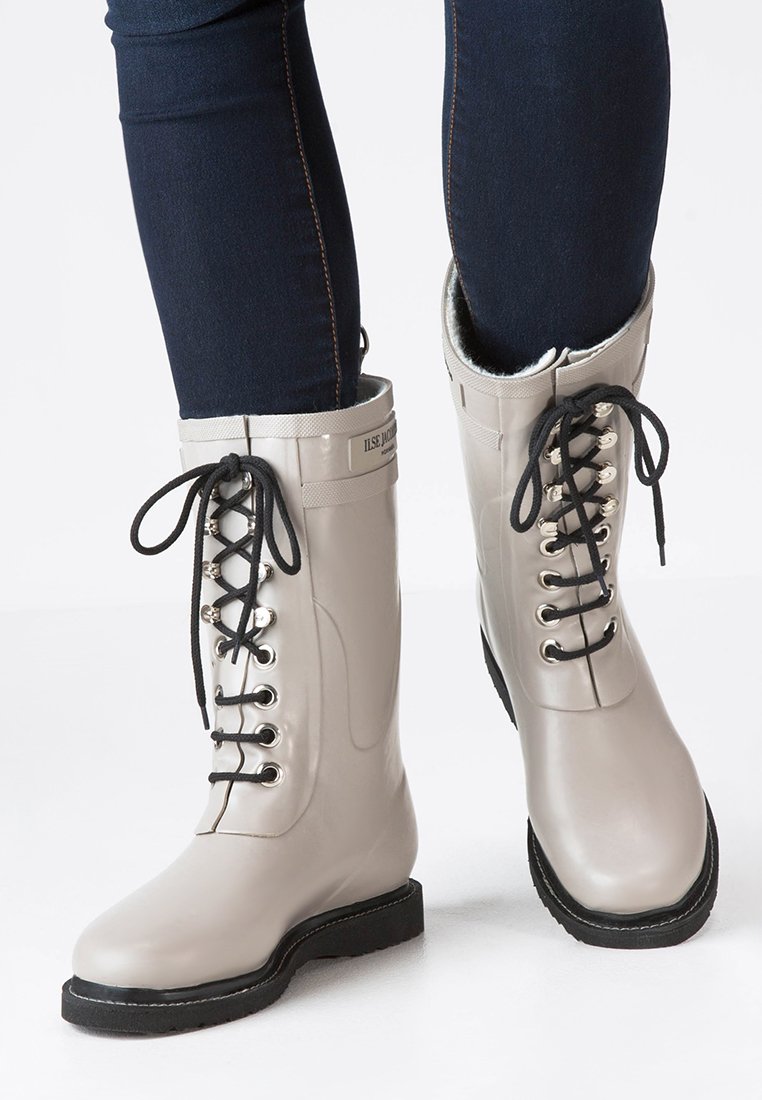 Bottes en caoutchouc grises à la cheville avec des lacets noirs, des œillets en argent et une semelle texturée noire. Doublées de matériau doux sur le dessus.