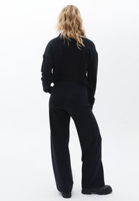 Svart oversized sweatshirt med avslappnad passform, i kombination med matchande svarta byxor med vida ben. Slät tyg med minimala detaljer och inga mönster.
