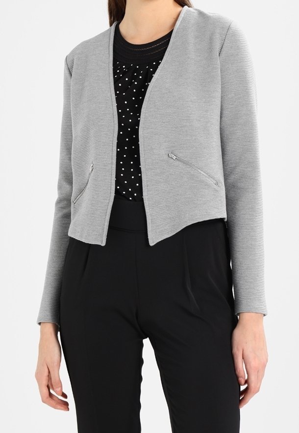 Szary skrócony żakiet z teksturowanej tkaniny. Posiada zapinane na zamek kieszenie i gładki dekolt, noszony na czarnej bluzce z kropkami i czarnych spodniach.