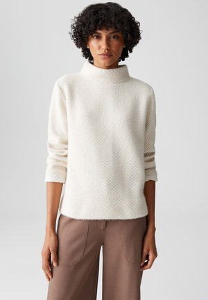 Crème kleurige pullover trui met een hoge hals, textuurstof en driekwart mouwen, gecombineerd met bruine wijde broek.