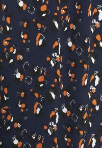 Marinfärgad tyg med ett abstrakt leopardmönster i svart, vitt och orange prickar, med varierande former och texturer i hela designen.