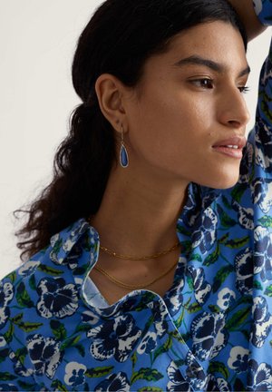 Blauw bloemenoverhemd met kraag, gelaagde gouden kettinkjes en een blauwe druppelvormige oorbel, met patronen en texturen.