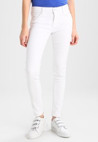 Jeans ajustados blancos con un diseño clásico de cinco bolsillos, hechos de tela de mezclilla. Combinados con zapatillas blancas que tienen tres tiras.