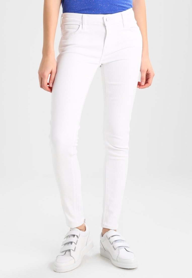 Jeans ajustados blancos con un diseño clásico de cinco bolsillos, hechos de tela de mezclilla. Combinados con zapatillas blancas que tienen tres tiras.