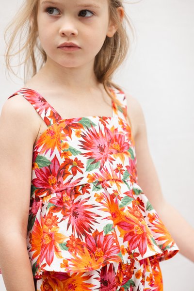 Αμάνικη μπλούζα με λουλούδια σε έντονα κόκκινα, πορτοκαλί και ροζ χρώματα σε λευκό φόντο, με λοξή τελείωμα και ρυθμιζόμενους ιμάντες.