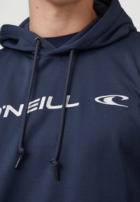 Mörkblå huvtröja i slätt tyg, med en framstående logo i vitt. Inkluderar justerbara snören och har en normal passform.