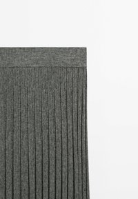 Tissu en maille côtelée grise avec une large ceinture, montrant des plis verticaux sur une surface plate avec un fond blanc.