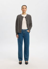 Šedý pletený kardigan s kulatým výstřihem a zapínáním na knoflíky, nošený přes krémový top; doplněný o modré džíny s vysokým pasem a černé baleríny.