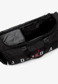 Sort duffelbag med en glat overflade, der har et stort rødt Jordan-logo, solide håndtag og et åbent rum, der viser et mørkt indre.