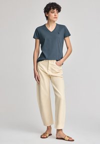 Marine V-hals T-shirt, beige rechte pantalons en bruine slippers. Soepele stof, casual pasvorm en minimale branding op het shirt.
