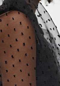 Zwarte doorschijnende overlay met kleine textuurpuntjes, die over een stevige donkere stof valt. Zachte, delicate materialen creëren een gelaagd effect.