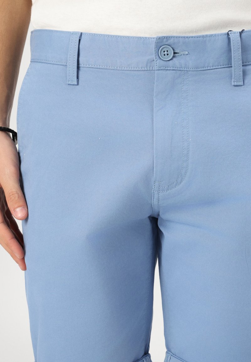 Helle blaue Baumwollhosen mit einer glatten Textur, ausgestattet mit einem Knopfverschluss und Gürtelschlaufen, die Details der Steppnähte der vorderen Taschen zeigen.