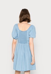 Vestido de denim azul claro com costas franzidas, mangas bufantes e saia até ao joelho. Design simples com decote redondo.