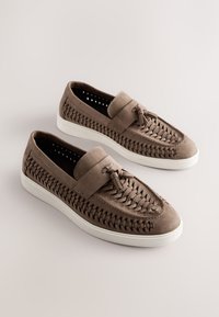 Brown leather slip-on shoes featuring woven detailing along the sides, flat white rubber soles, and a textured toe cap.