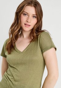 T-shirt vert olive en tissu léger, avec des manches courtes et un col en V orné de couture décorative le long de l'encolure.