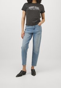Camiseta gris de manga corta con estampado "TOMMY JEANS NEW YORK CITY", combinada con jeans ajustados de color azul claro y mulas negras con punteras puntiagudas.