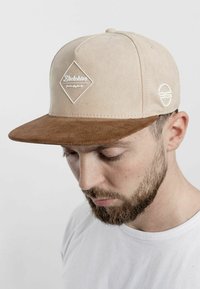 Beige suede cap with a brown corduroy peak, featuring a white diamond logo and an embroidered circular logo on the side.