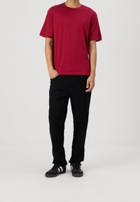 Camiseta de algodón roja con cuello redondo, combinada con pantalones negros de corte holgado. Zapatillas negras con franjas blancas completan el look.