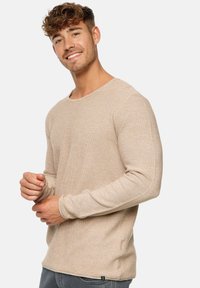 Beige pitkähihaine neulepaita pyöreällä pääntiellä, tekstuuripinnoitteella ja slim fit -mallilla. Sisältää pienen logotagin vasemmassa alakulmassa.