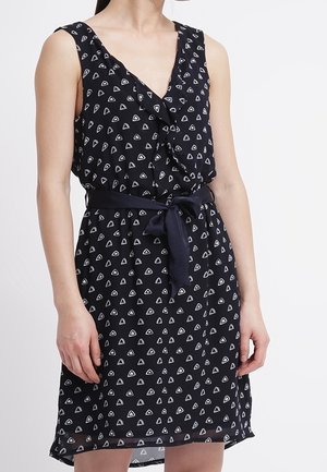 Robe sans manches bleu marine avec un décolleté en V, ornée d'un motif géométrique en triangles blancs et d'une ceinture nouée pour une silhouette définie.