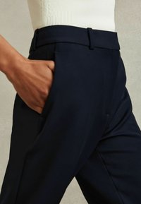 Pantaloni tailored blu con una texture liscia, dotati di tasche laterali e una vita aderente. Il tessuto appare morbido e strutturato.