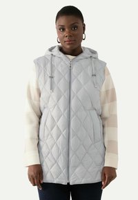Ljust grå quiltad väst med huva, framslutning med dragkedja och justerbara snoddar, med två sidofickor. Bärs över en randig långärmad topp.
