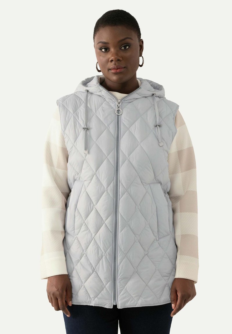 Ljust grå quiltad väst med huva, framslutning med dragkedja och justerbara snoddar, med två sidofickor. Bärs över en randig långärmad topp.