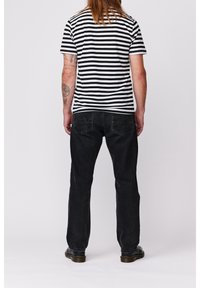 Camisa de rayas en blanco y negro combinada con jeans negros. La camiseta tiene mangas cortas y un cuello redondeado. Los jeans tienen bolsillos traseros y un corte relajado.