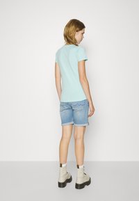 Šviesiai mėlynas trumpomis rankovėmis marškinėliai poruoti su šviesiais džinsiniais šortais, kurių kraštai sukrauti, papildyti smėlio spalvos auliniais batais su juodomis padangomis.