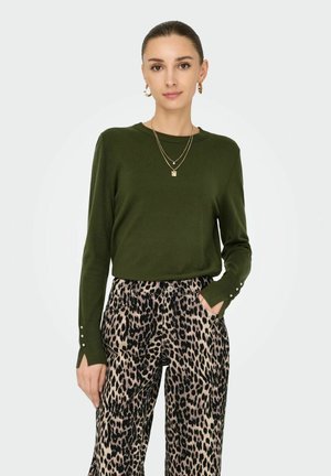 Pull olive green à manches longues avec des accents de boutons subtils sur les manches, associé à un pantalon large à imprimé léopard avec poches.