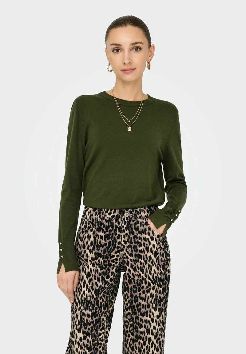Maglione verde oliva a maniche lunghe con sottili dettagli di bottoni sulle maniche, abbinato a pantaloni a gamba larga con stampa leopardata e tasche.