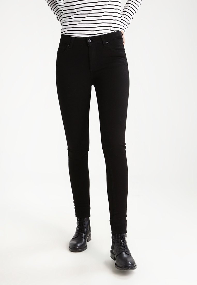 Jeans skinny de mezclilla negra con una textura suave, cintura media, cinco bolsillos y trabillas para cinturón, combinados con botas negras con cordones.