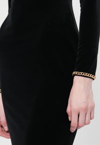 Black velvet dress with long sleeves, fitted silhouette. Gold chain bracelet on wrist. Smooth texture, minimalistic design.