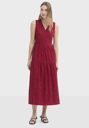 Robe rouge sans manches avec un décolleté en V et une jupe à volants. Présente un tissu texturé et un détail de ceinture nouée, atteignant le milieu du mollet.