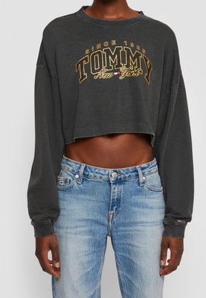 Sweatshirt noir coupé à manches longues, arborant "TOMMY New York" en lettres dorées. Associé à un jean en denim bleu clair.