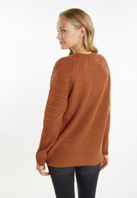 Rozsdabarna kötött pulóver texturált kábelmintázattal, bordás mandzsettákkal és szegéllyel, amely laza szabású és kerek nyakú.