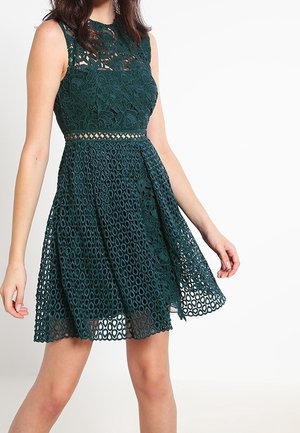 Robe en dentelle verte avec un corps semi-ajusté, motif floral, sans manches et une jupe évasée avec des découpes circulaires.
